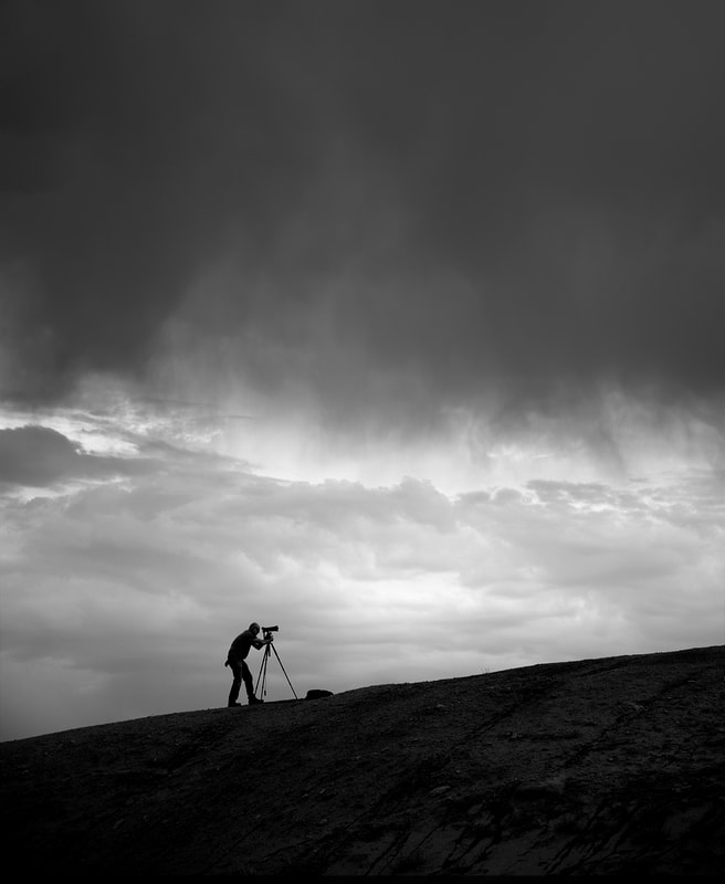 Black and White image of silhouette of photographer on ridge during storm